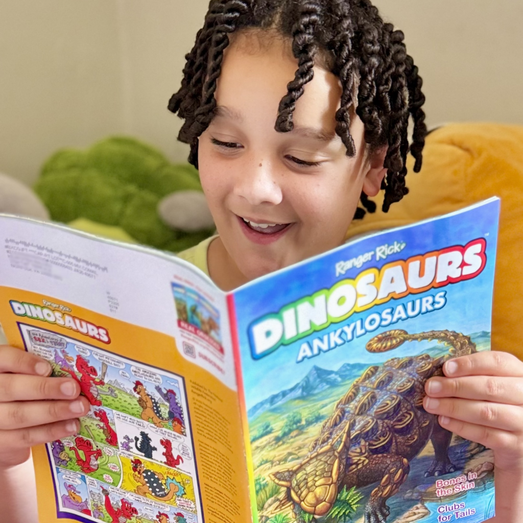 excited child smiling while reading a dinosaur book showing how interest motivates reading regardless of level